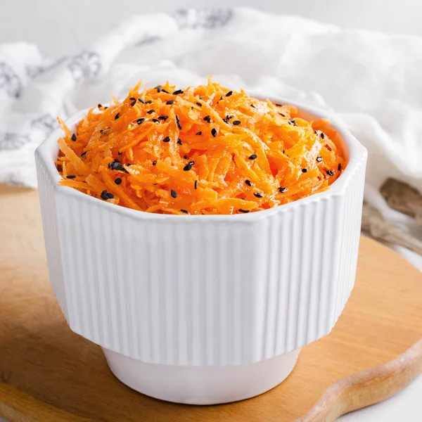 Пряный морковный салат с семенами кунжута в белой миске на шерстяной доске . — стоковое фото