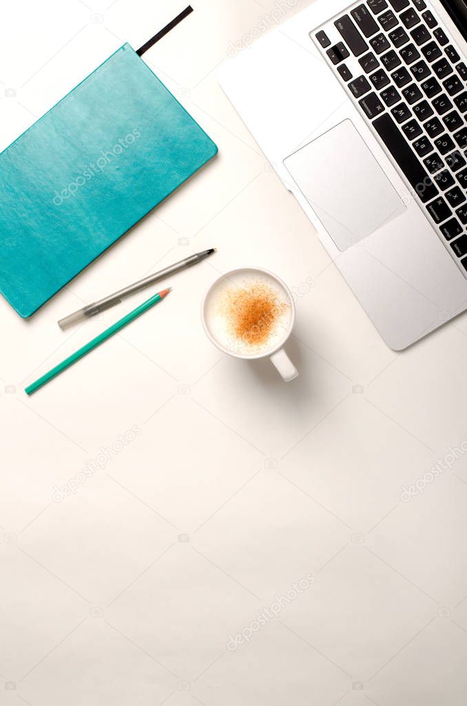 Work space with laptop, turquoise notebook and cinnamon coffee on white table. Flat lay, top view