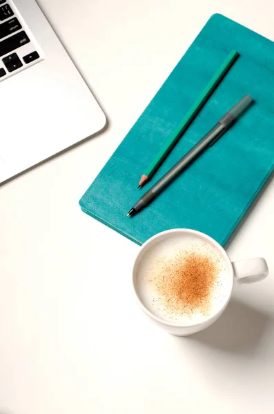 Miejsce do pracy z laptopem, turkusowym notebookiem i cynamonową kawą na białym stole. Widok z góry — Zdjęcie stockowe