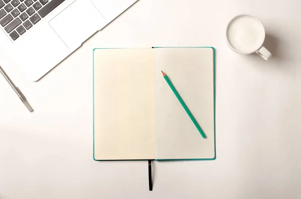 Espaço de trabalho com laptop, caderno turquesa e cappuccino na mesa branca. Depósito plano Imagem De Stock