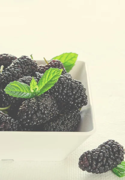 Mulberries maduras frescas com hortelã em tigela sobre fundo branco, espaço cópia Imagem De Stock