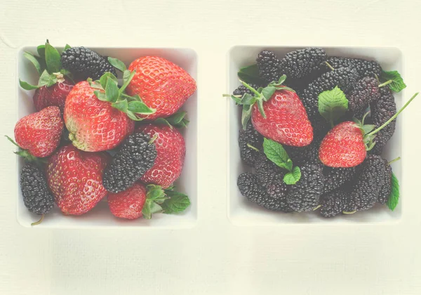 Mulberries maduras frescas e morangos com hortelã em tigela sobre fundo branco, espaço cópia Fotografia De Stock