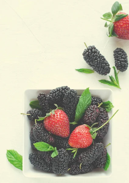 Mulberries maduras frescas e morangos com hortelã em tigela sobre fundo branco, espaço cópia Fotografia De Stock