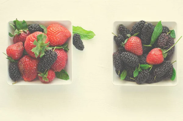Mulberries maduras frescas e morangos com hortelã em tigela sobre fundo branco, espaço cópia Fotografias De Stock Royalty-Free