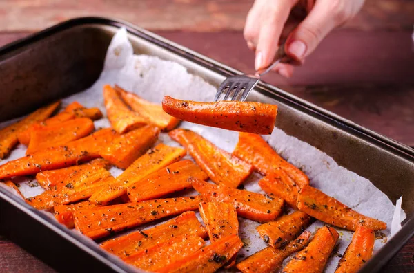 PIece van geroosterde gekarameliseerde biologische wortelen met specerijen op vork in de hand — Stockfoto