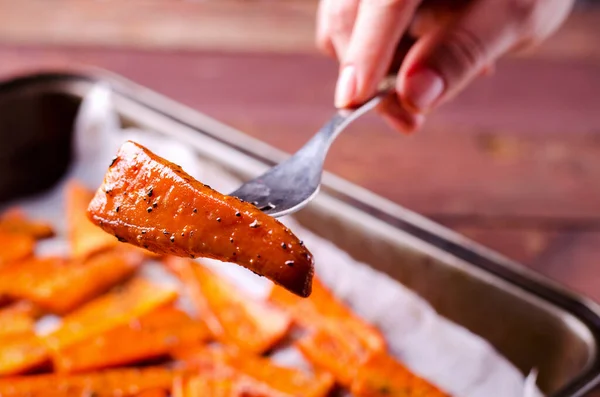 PIece van geroosterde gekarameliseerde biologische wortelen met specerijen op vork in de hand — Stockfoto