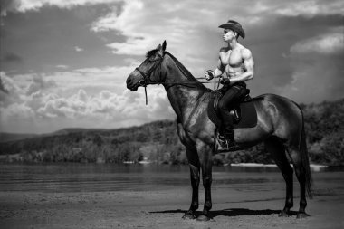 Maço erkek yakışıklı kovboy arka planda gökyüzü ve su ata binme.