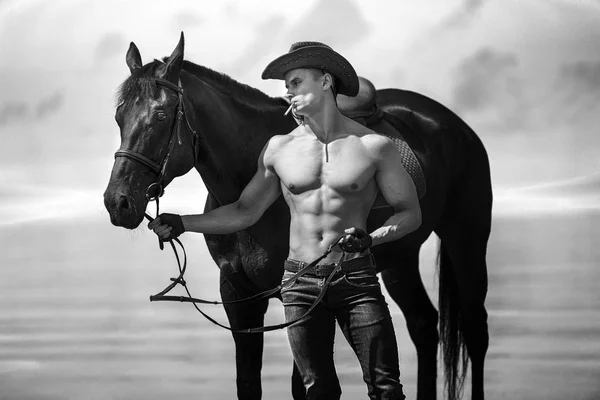 Macho man handsome cowboy and horse on the background of sky and water. — Stock Photo, Image