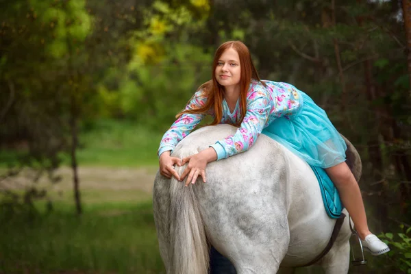 Руда дівчина і білий кінь в лісі — стокове фото