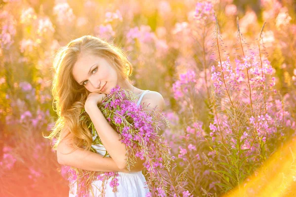 若い美しいブロンドの女の子は 日没時に春の開花フィールドにピンクの花を集めます 自然の化粧品を宣伝するための美しさ 新鮮さ 若さと健康の概念 ストック画像
