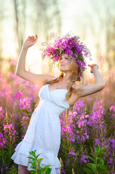 화환을 머리에 아름다운 금발의 소녀는 꽃피는 들판에서 분홍빛 모은다 — 스톡 사진