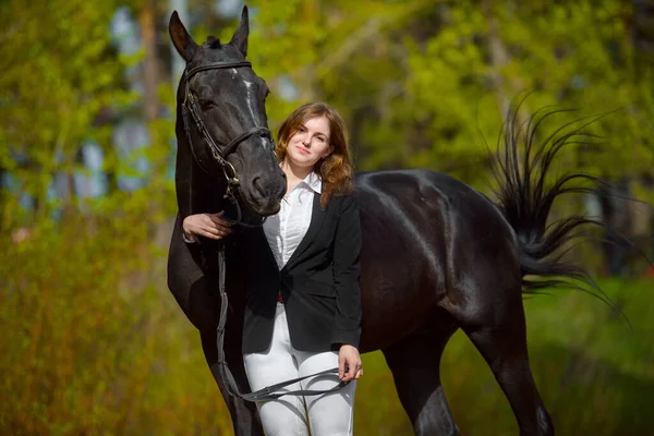 年轻的女孩骑着一匹黑马在春天的户外场景 — 图库照片