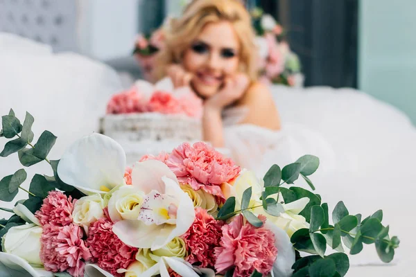 Beautiful wedding bouquet lies on a light floor in a room full of light, in the background is a beautiful bride with a wedding cake