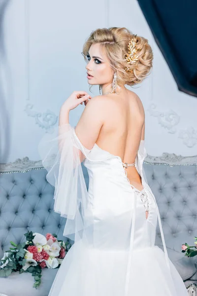 Όμορφη νύφη με τα μαλλιά και το μακιγιάζ που ταιριάζει γαμήλιο φόρεμα με δέσιμο πίσω και μια γαμήλια ανθοδέσμη στο παρασκήνιο — Φωτογραφία Αρχείου