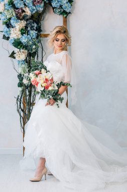 Gelin buketi ve ellerinde çiçeklerle bir duvar bir arka plan üzerinde ayakkabı ile gelinlik