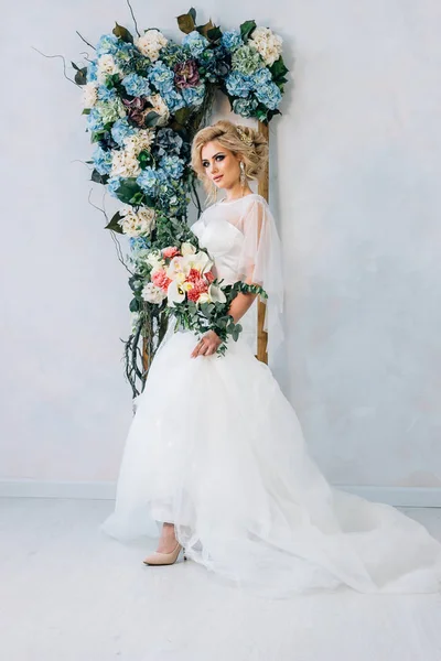 Gyönyörű menyasszony, menyasszonyi ruha és cipő a csokor a kezében, a háttérben a falra virággal, vonat kialakítása — Stock Fotó