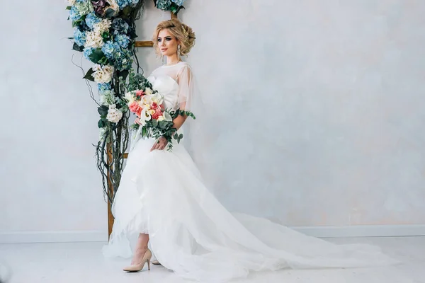 Наречена у весільній сукні з букетом в руках на фоні стіни з квітами — стокове фото