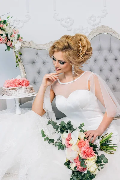 Η όμορφη νύφη γαμήλιο χτένισμα και make-up κοντά ένα κέικ με μια ανθοδέσμη στα χέρια — Φωτογραφία Αρχείου