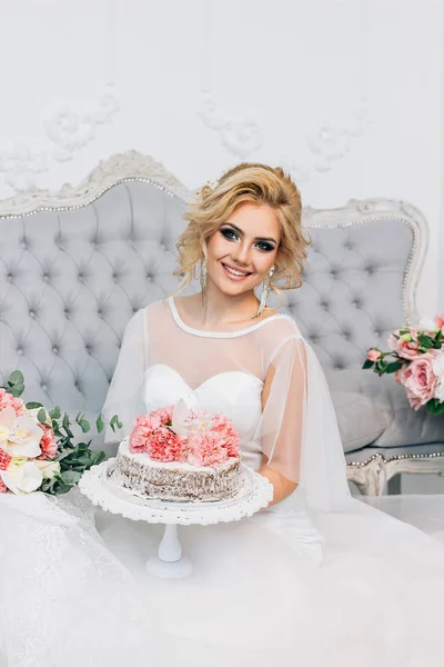 Όμορφη ξανθιά κοπέλα κάθεται και κρατώντας μια γαμήλια τούρτα στα χέρια — Φωτογραφία Αρχείου