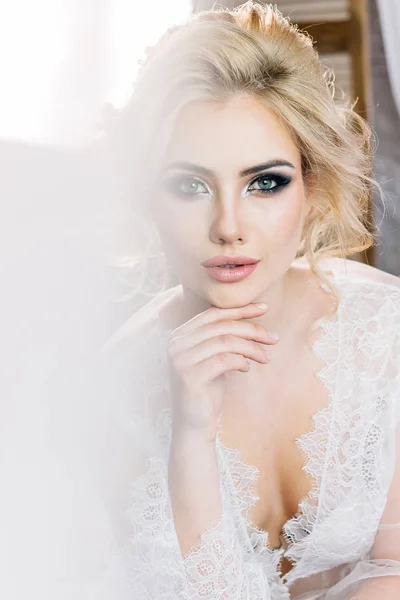 Portrait of a beautiful blond girl in a negligee with a beautiful hairdo and makeup