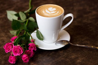 bir masada koyu kahverengi, yanında bir Çin pembe Gül gül, güzel dekore edilmiş cappuccino kahve