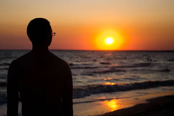 Silhouette eines Mannes mit Brille, in den Strahlen der untergehenden Sonne am Meer. unter den Text legen, sich am Meer entspannen — Stockfoto