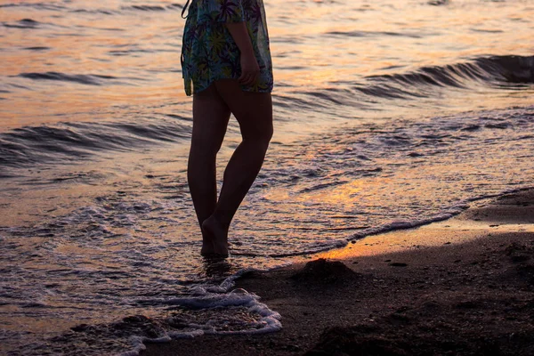 Крупный план босых ног девушки, идущей по пляжу на закате, с волновой кромкой, нежно вспенивающейся под ними, тонированные цвета — стоковое фото