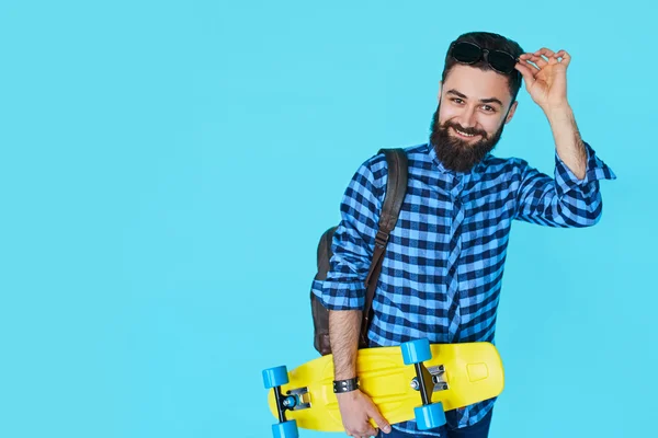 화려한 파란색 배경에 노란색 스케이트 보드를 들고 hipster 남자 — 스톡 사진