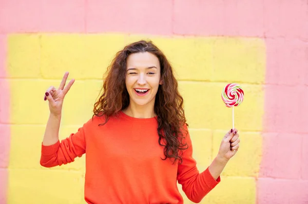 Pretty woman in summer clothes showing peace and holding lolipop — Stock Photo, Image