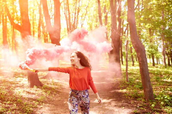 Glad tjej skrattar och kör med rosa färg rök bomb i skogen. — Stockfoto