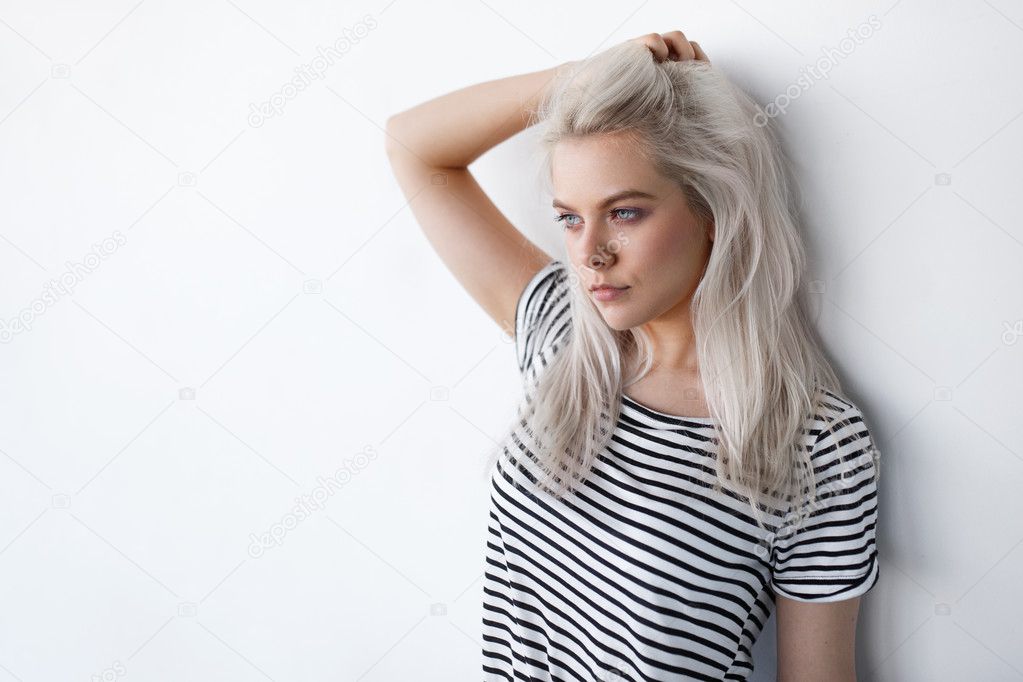 beautiful young blond woman posing while leaning on white wall