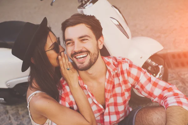 Couple whipsering to ear a secret while sitting near scooter — Stock Photo, Image