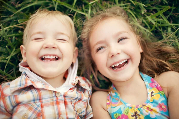 Yeşil çim üzerinde yalan çocuklar mutlu iki görünüm portre üzerinde gülümseyen. — Stok fotoğraf
