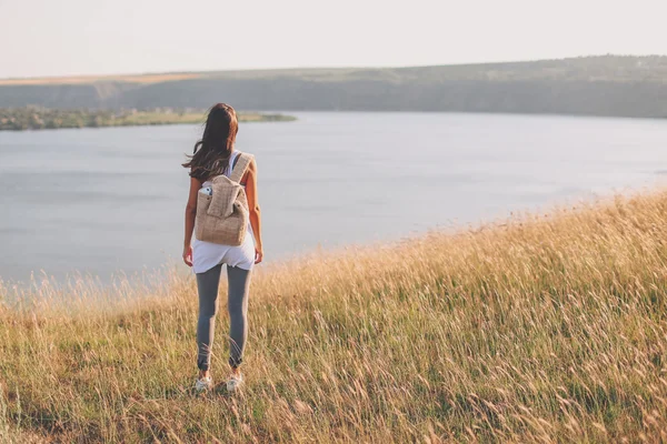 Hipster young girl with backpack enjoying view on cliff. — Stock Photo, Image