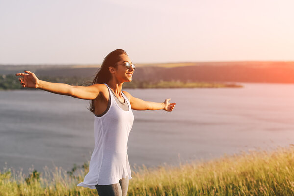 Successful sporty woman raising arms towards golden beautiful sunset