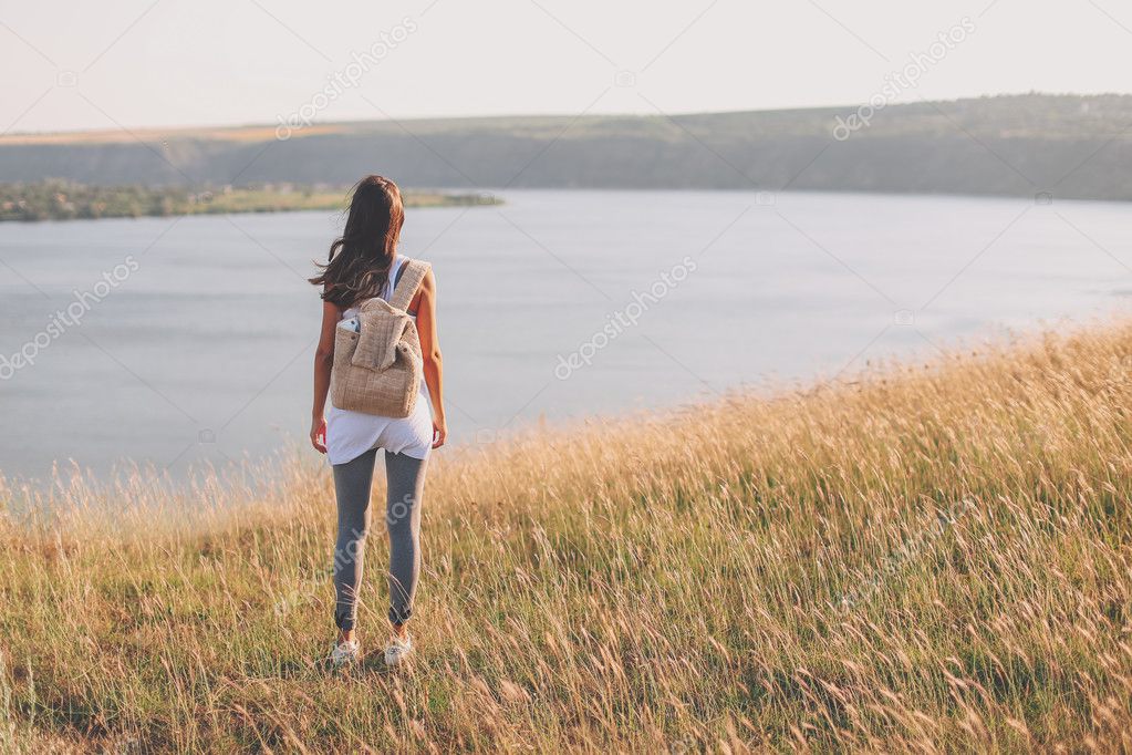 Hipster young girl with backpack enjoying view on cliff.