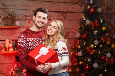 Mutlu çift gülümseyen ve büyük kırmızı hediye kutusu tutarak kış pullovers
