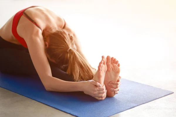 Profile shot of young woman stretching to touch her toes while sitting against white background — Stock Photo, Image