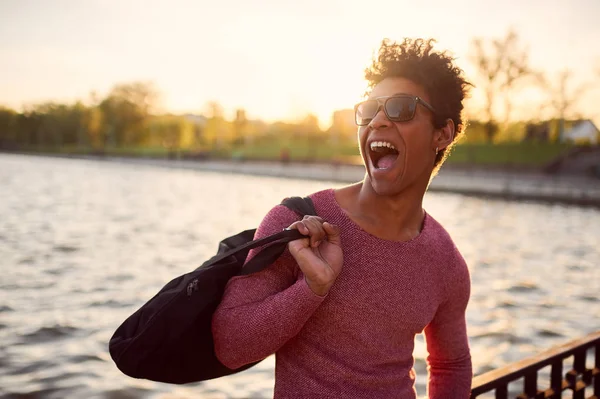 Весёлый студент в солнечных очках, улыбающийся у озера — стоковое фото