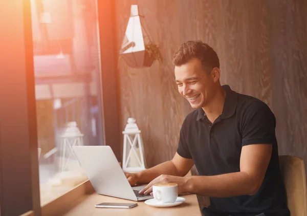 Предприниматель улыбается во время работы за ноутбуком в солнечном кафе — стоковое фото