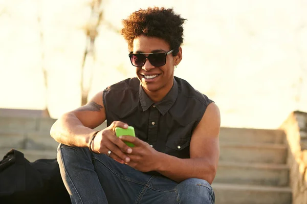 Nowoczesny czarny młody człowiek uśmiechający się podczas pisania wiadomości — Zdjęcie stockowe