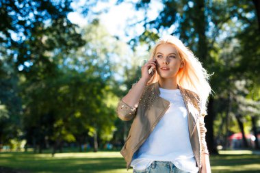 Genç kadın parkta yürürken smartphone kullanır