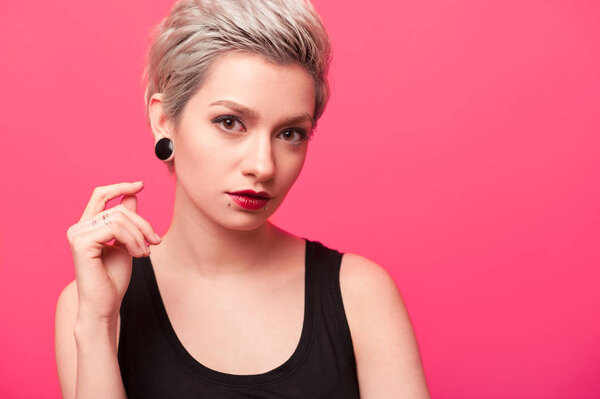 Hipster girl with blond hair and piercing over pink background