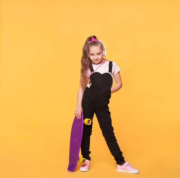 Malé školy dívka pózuje s skateboard a sluchátka — Stock fotografie