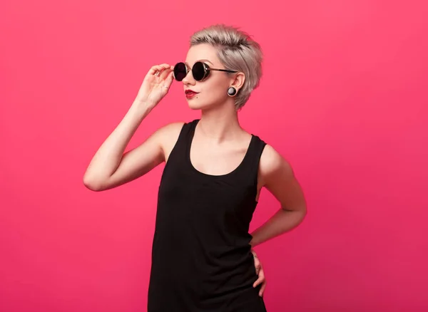 Mujer atractiva joven con gafas de sol redondas sobre fondo de color rosa — Foto de Stock