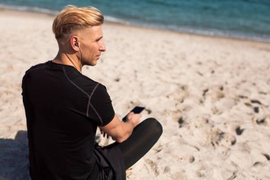 Smartphone ile sahilde oturan adam