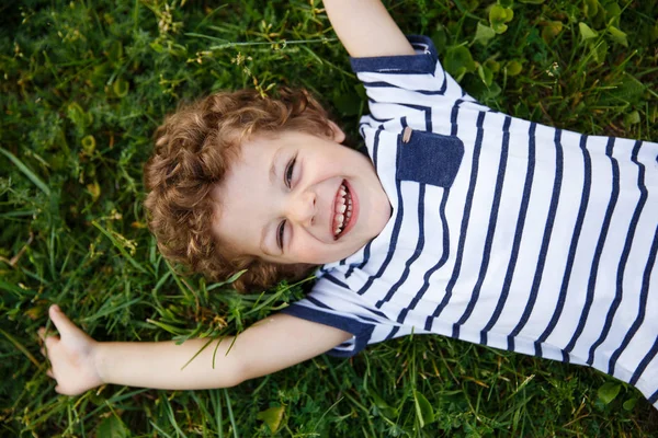 Усміхнений хлопчик лежить на зеленій траві — стокове фото