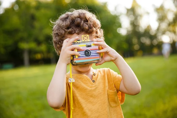 Молодий хлопчик тримає камеру, стоячи в парку — стокове фото