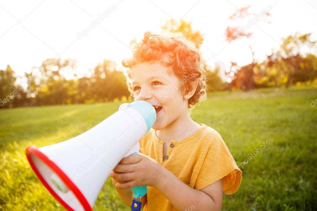 Boy standing in field speaking in megaphone