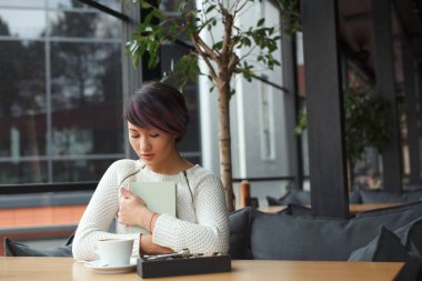 Masada otururken kitap tutan kız